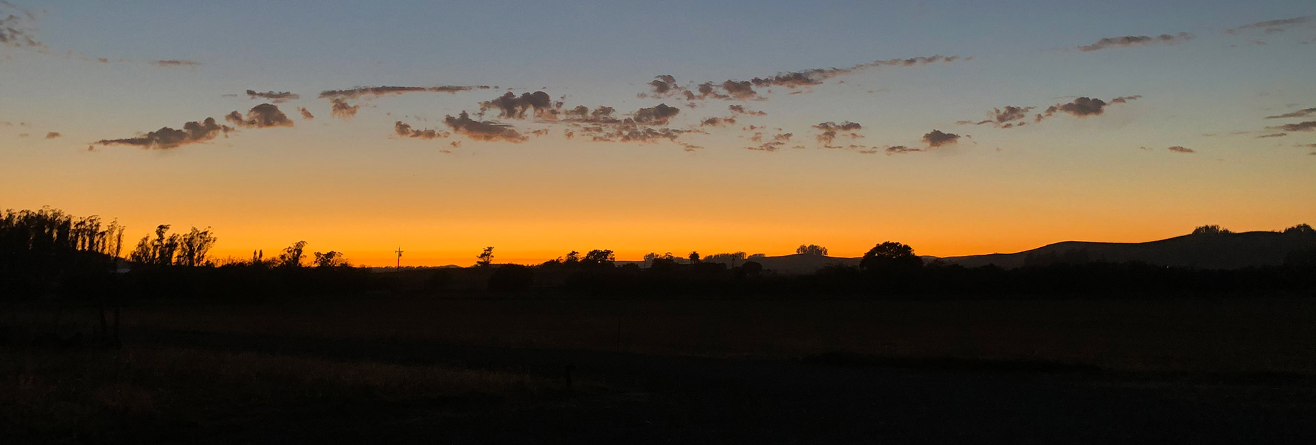 View of the sun that has gone down on the farm with some clouds in the sky